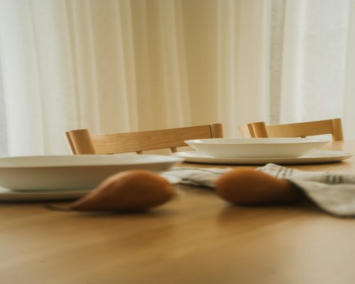 A wooden family dining table set with white ceramic plates and fresh organic vegetables
